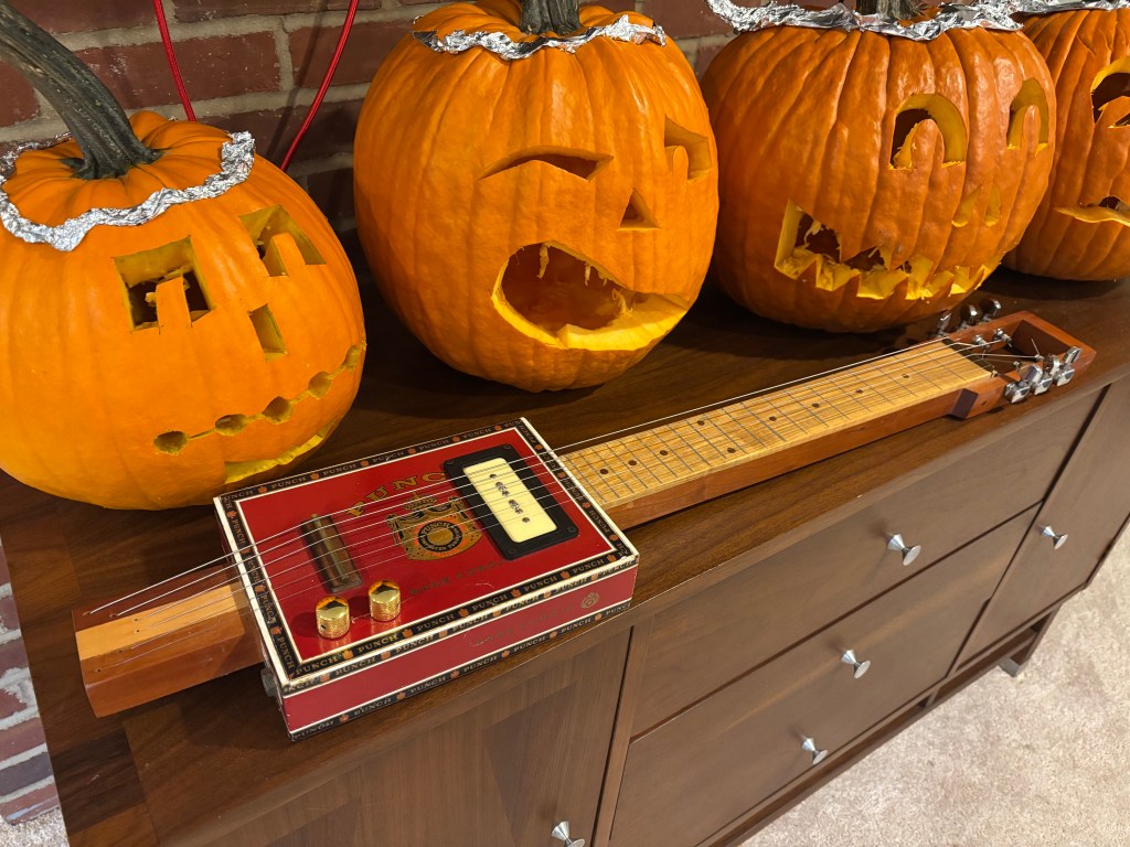 Cigar box lap steel guitar with C.B. Gitty P-90 soapbar pickup, posed in front of Jack-'o-Lanterns. 